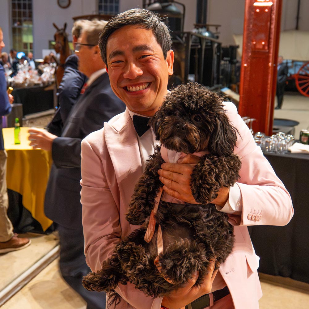 Person in tuxedo holding small brown dog.