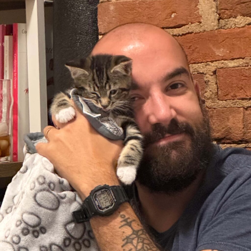 Man with beard snuggling with kitten in blanket.